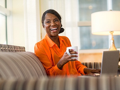 Woman in orange shirt smiling while drinking tea on couch
