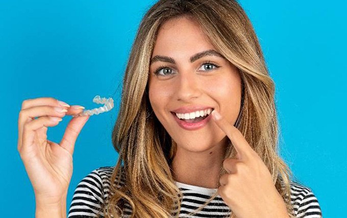 Young woman holding aligner and pointing to smile