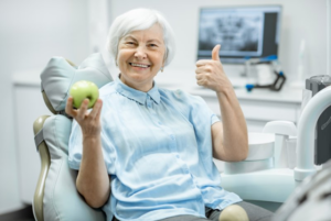 Woman holding an apple and smiling while waiting for her dental implant surgery